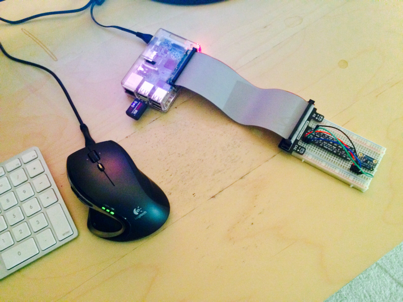 A Raspberry Pi wired by a ribbon cable to a small sensor breakout board on a desk, beside a keyboard and mouse.